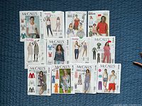 Overview of twelve uncut sewing pattern envelopes on blue surface