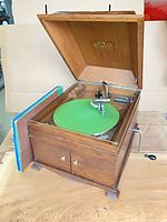 Gramophone open showing turntable, tonearm, records, crank