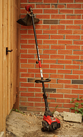 Full view of red and black Yard Machines gas trimmer leaning against brick wall