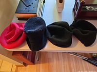 Four hats laid out side by side: red beret, black beret, two black beanies