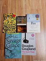 All five paperback books laid out on wooden floor: Savage Grace, The Party Wall, Invisible Man, Ru, The Gum Thief