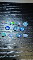Eleven oval opal cabochons on dark surface showing play of color