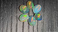 Six oval opal cabochons arranged on textured black background showing play-of-color