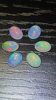 Six oval cabochon opals on black textured surface