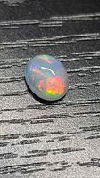 Oval cabochon opal on dark surface showing multicolor flashes