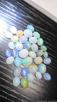 Group of oval cabochon opals on black surface
