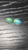 Two oval cabochon opals displaying green and orange flashes
