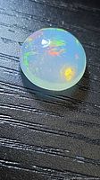 Round crystal opal cabochon on black surface showing play of color