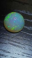 Round opal cabochon showing multi-color play-of-color on black background