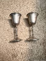 Two tarnished silver-plated goblets lying on carpet