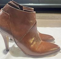 Side view of both brown leather ankle boots showing pointed toes, heels and side zipper