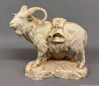 Front view of off-white resin goat figurine, curved horns, money bag on back, log base visible