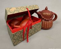 Large script teapot beside open box holding miniature set