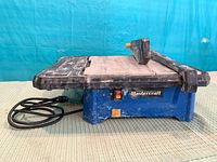 Left side view of Mastercraft wet tile saw showing blue base, black deck, power cord