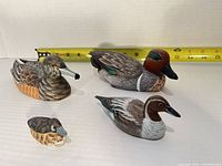 Front view of four carved wooden duck figurines with tape measure for scale