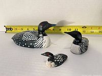 Three wooden loons with tape for scale