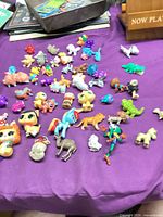 Overview of mixed plastic animal and character figures spread on purple cloth