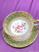 Teacup nested on saucer showing interior rose motif, green and gold decoration