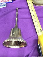 Side view of brass hand bell showing scalloped rim and ruler for scale