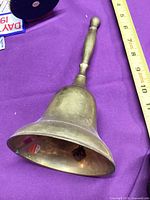 Full view of brass hand bell showing size against ruler