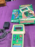 Handheld game, box, instruction sheet, AC adapter visible