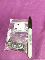 Three black rubber wheels in a resealable bag with a marker beside for scale