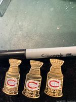 Front view of three identical Montreal Canadiens Stanley Cup lapel pins beside Sharpie for scale