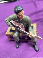 Front view of soldier figurine seated on trunk playing guitar