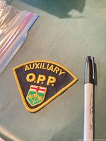 Front of triangular O.P.P. Auxiliary embroidered patch beside marker for scale