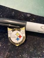 Front of Pittsburgh Steelers shield pin beside marker for scale