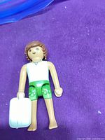 Playmobil figure lying on purple surface holding suitcase