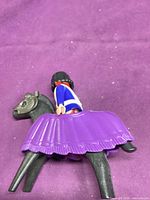 Playmobil figure seated on black horse with purple skirt saddle