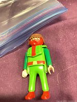Front view of Playmobil figure showing green outfit, red accents, brown hair