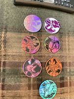 Seven holographic Pokemon coins arrayed on plaid surface