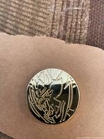 front of round black enamel Pokémon pin with gold outline character