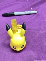 Front view of Pikachu figure showing face, ears and translucent tail with Sharpie for scale
