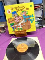 Front cover of Strawberry Shortcake Sweet Songs LP on stand with vinyl record and inner sleeve displayed