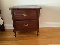 Front view of one nightstand showing two drawers, brass pulls, cabriole legs