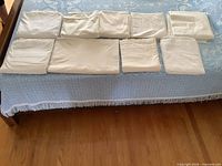 Nine folded off-white queen flat sheets laid on bed