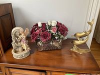 All three items on wooden surface: angel fountain figurine, floral basket, brass dolphins