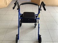Front view of blue rollator walker showing seat, bag, wheels, and hand brake handles