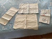 Group view of five embroidered pillowcases on bed surface