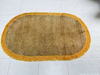 Full view of oval brown-tan rug with gold fringe