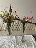Two tall clear glass vases with artificial arrangements on table