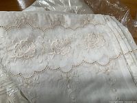 Close-up of embroidered floral pattern and scalloped lace edge on ivory sheer fabric