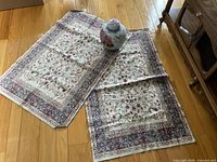 two small floral Persian-style rugs laid on floor with ginger jar placed on top
