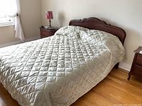 Full view of queen bed with quilted bedspread and wood headboard/footboard