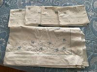 Folded queen sheet with four pillowcases showing blue hand embroidery