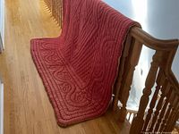 Full view of quilt draped over railing showing red side and overall size