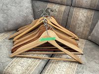 Stack of mixed-finish wooden hangers with metal hooks on sofa